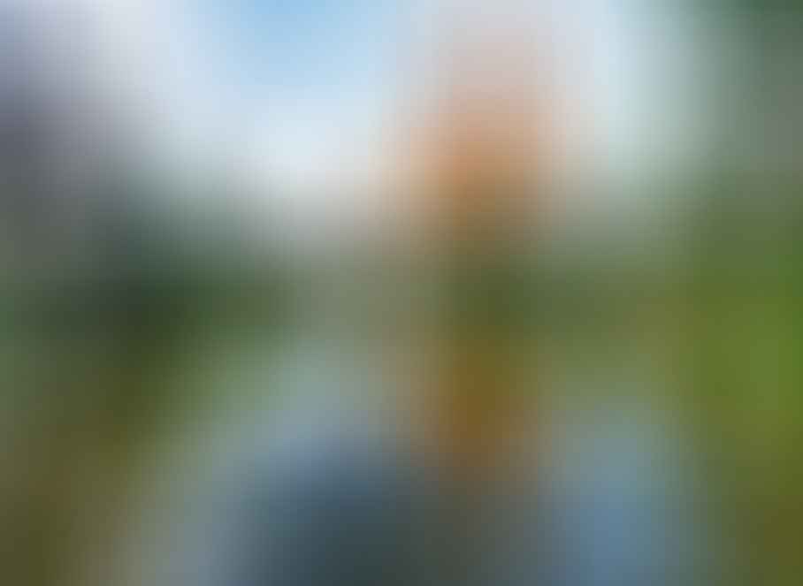 The Sagrada Familia basilica in Barcelona is reflected in a pond, surrounded by trees under a partly cloudy sky.