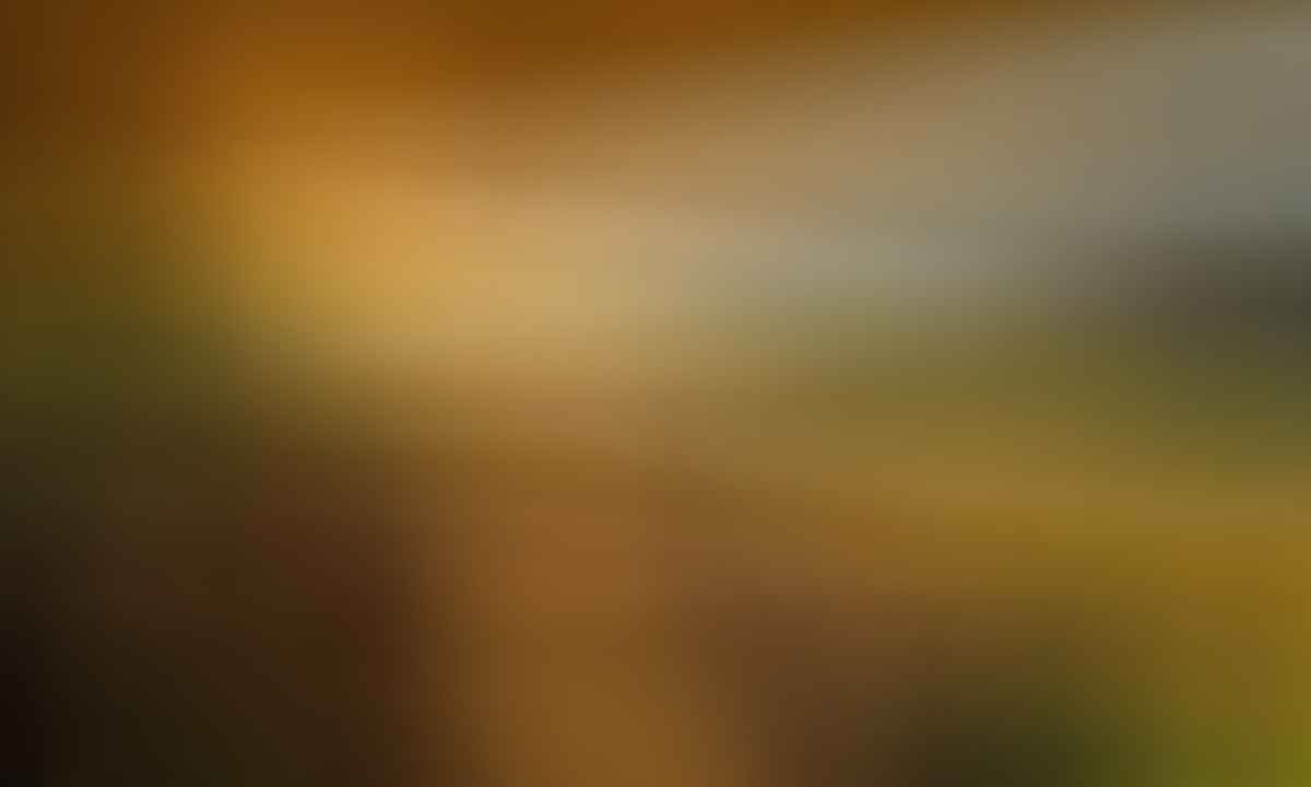 A covered patio with a couch and table overlooks a river, grassy shore, and distant hills at sunset.