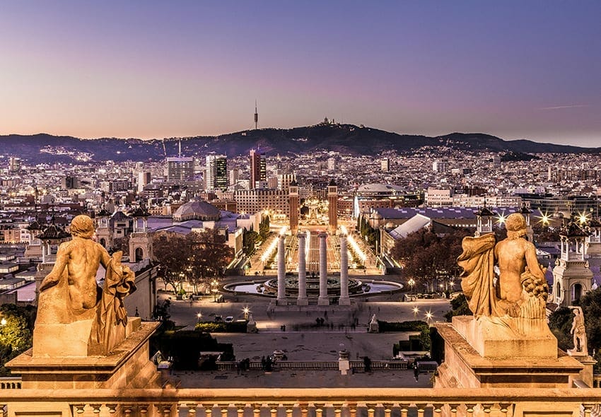 View of Barcelona at dusk from the steps of the National Art Museum, with city lights, statues in the foreground, and Montjuïc hill in the background—a perfect moment on a Spain & Portugal Private Luxury Tour.