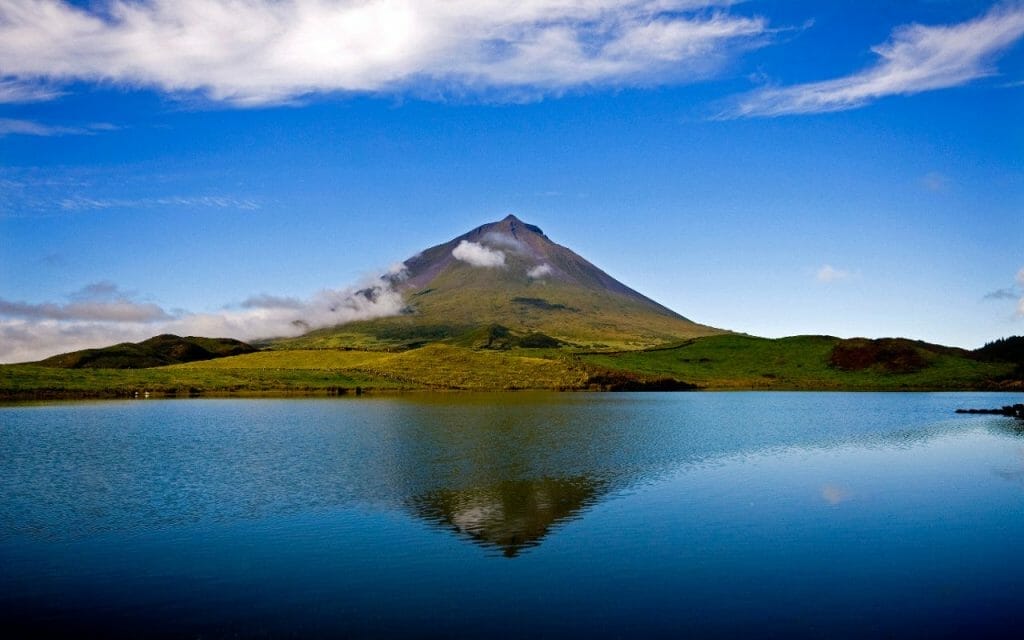 Volcanic cone of Mount Pico rising above green hills and reflected in a still lake, Pico Island, Azores, Portugal