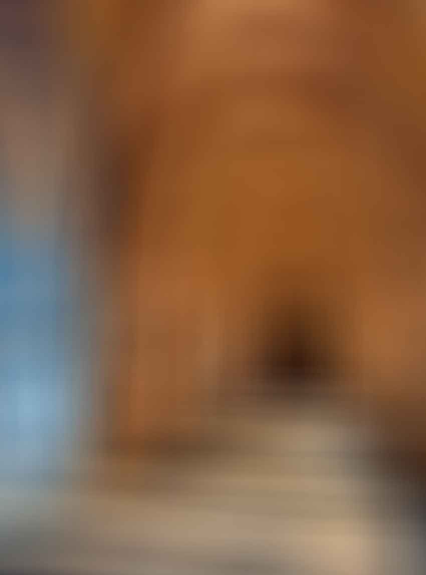 Stone hallway with arched ceilings, decorative columns, and blue-and-white tile murals on the left wall, illuminated by sunlight streaming through arches.