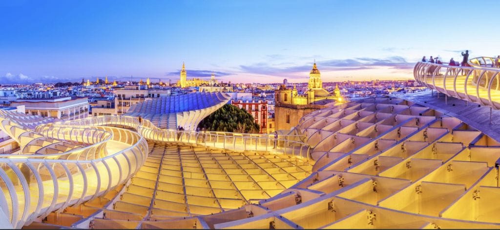 A wide view of the Metropol Parasol’s wooden structure in Seville, Spain, with the city skyline and historic buildings visible at sunset.