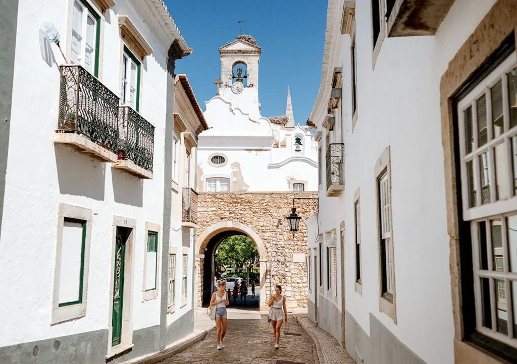 Arched stone gateway with a bell tower above, opening onto a whitewashed street in an Algarve old town, Portugal