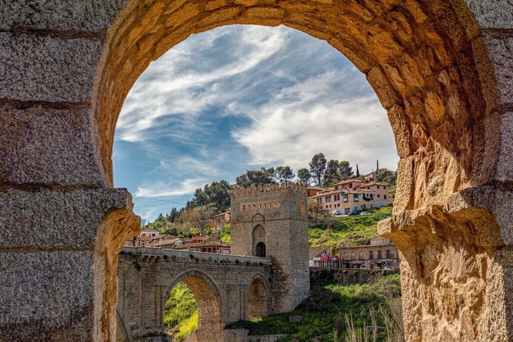 Stone arch framing a medieval bridge and gate over the Tagus, Toledo, Spain