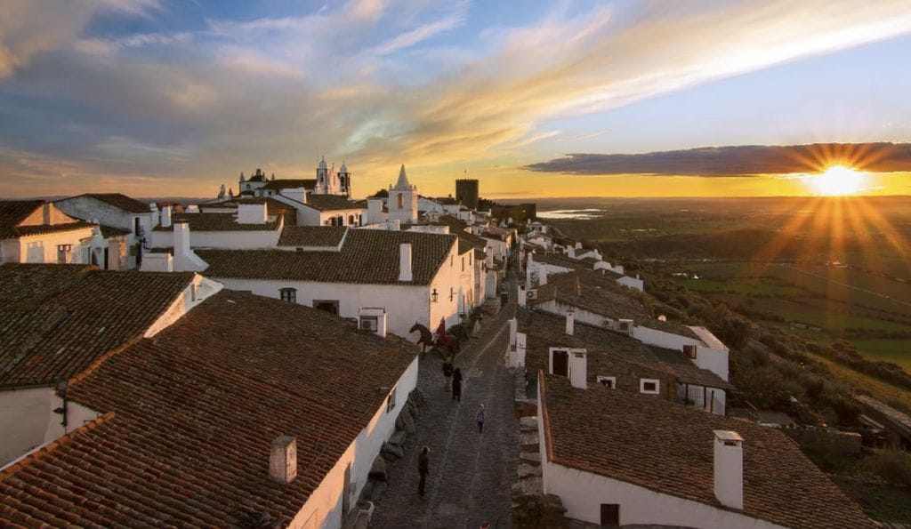 Whitewashed houses and terracotta roofs along a sloping street at sunset in a hilltop village of the Alentejo, Portugal