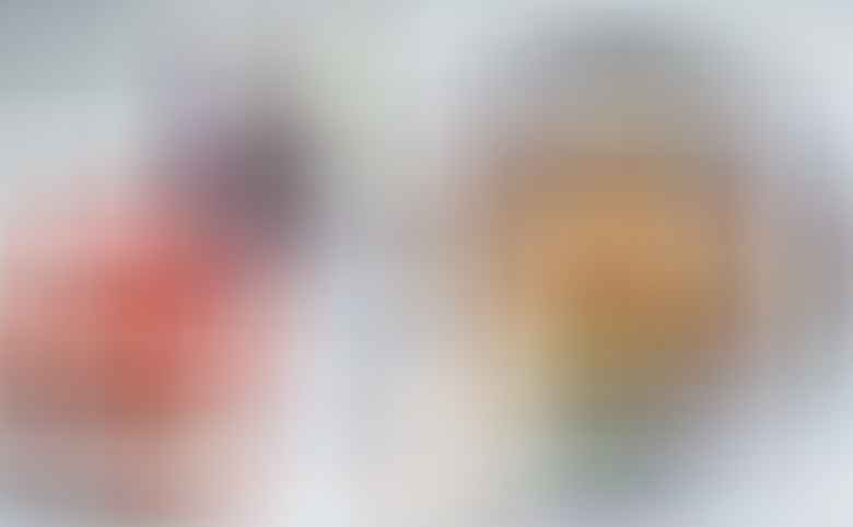 A bowl of baba ganoush garnished with pomegranate seeds, olive oil, and parsley sits next to a piece of pita, a whole eggplant, and a split pomegranate on a mosaic surface.