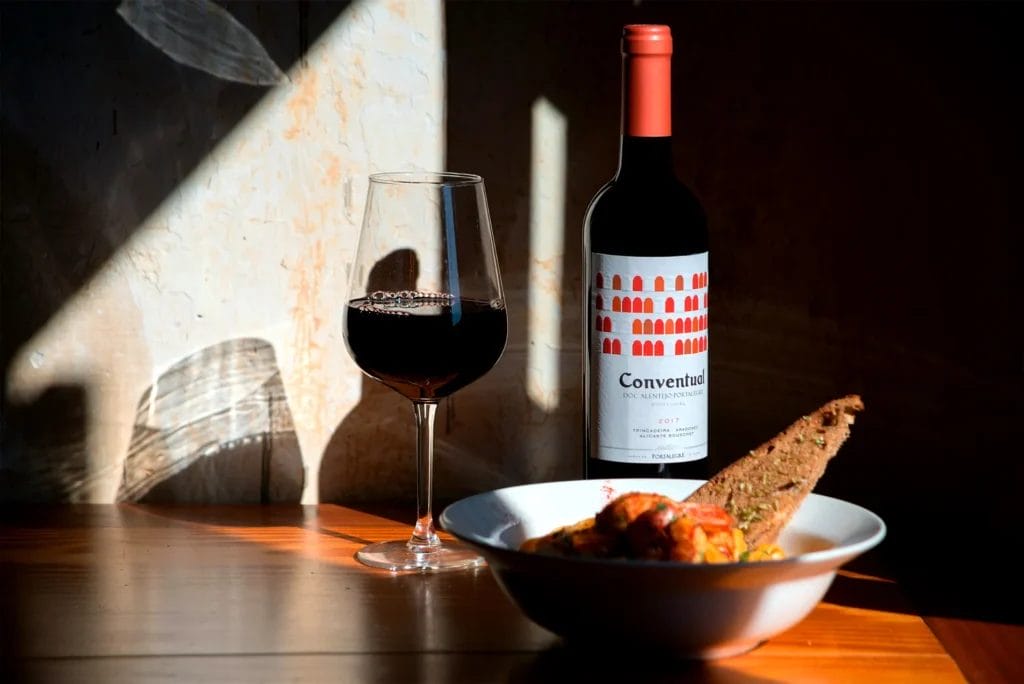 Bottle of red wine, a glass and country bread on a wooden table in warm evening light
