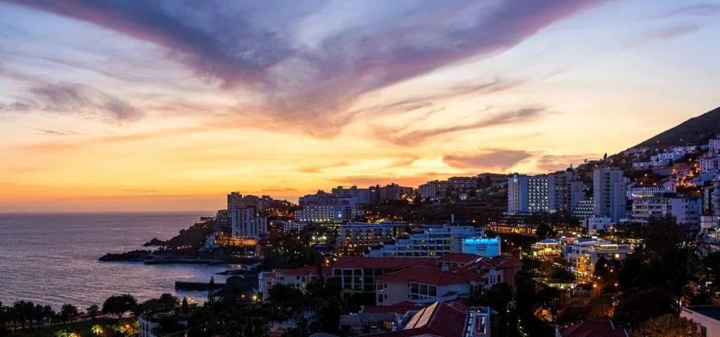 Sunset over Madeira's south coast, with the lights of hillside hotels and homes above the Atlantic, Portugal