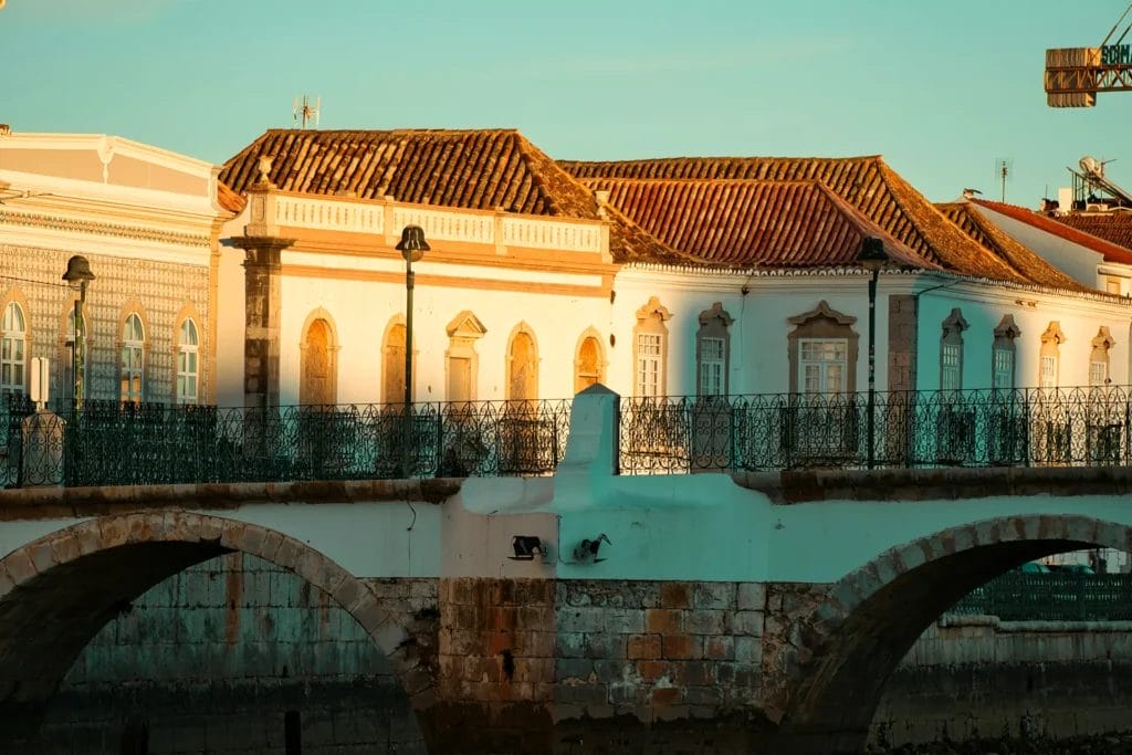 Arches of the old bridge over the Gilão River below tiled-roof townhouses in warm evening light, Tavira, Algarve, Portugal